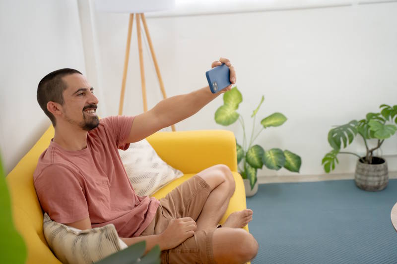  Homme souriant sur un canapé, en visioconférence avec la femme qu’il aime à distance