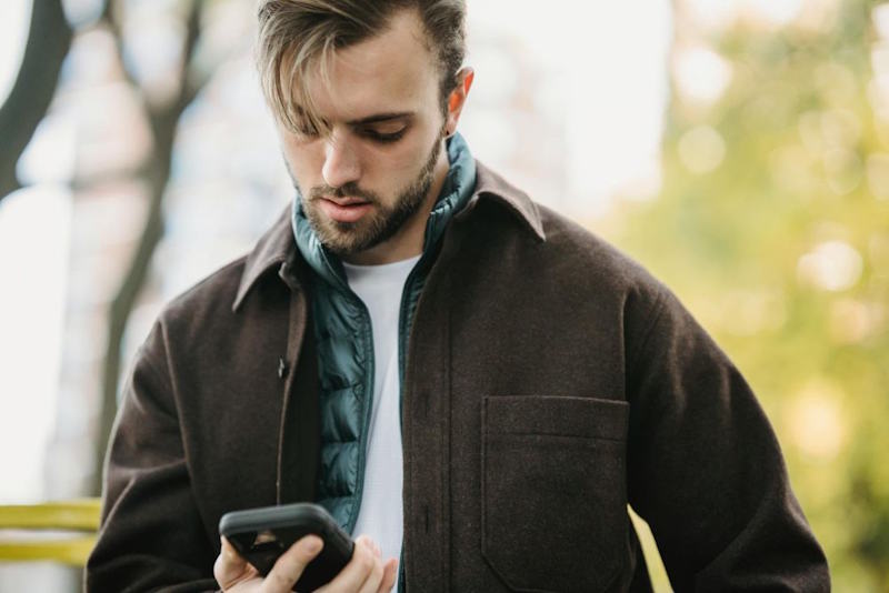 Homme pensif regardant son téléphone, symbole du manque dans une relation à distance.